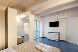 A modern hotel room with a large bed, a wardrobe, a television, and a bathroom visible through a glass door.