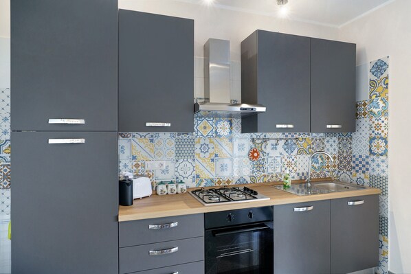 Una cocina con armarios grises, una estufa a gas, un horno empotrado y salpicadero de azulejos.