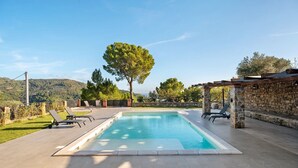 Una piscina con sillas de descanso, un muro de piedra y vistas a las colinas.
