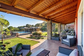 Un patio cubierto con mobiliario exterior, una piscina y vistas del paisaje circundante.