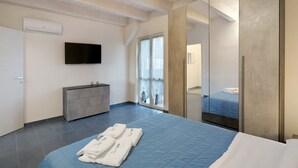 Moderni hotellihuone, jossa on suuri sänky, taulutelevisio, lipasto ja lasiliukuovi, joka johtaa parvekkeelle.
