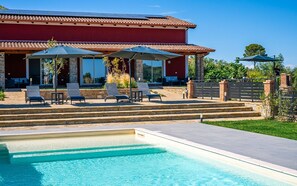 A pool with clear blue water, a red building with a tiled roof, and outdoor seating with umbrellas. - Apartment 'Appartamento Vite Vista Piscina' with Sea View, Wi-Fi and Air Conditioning (Montecorice)