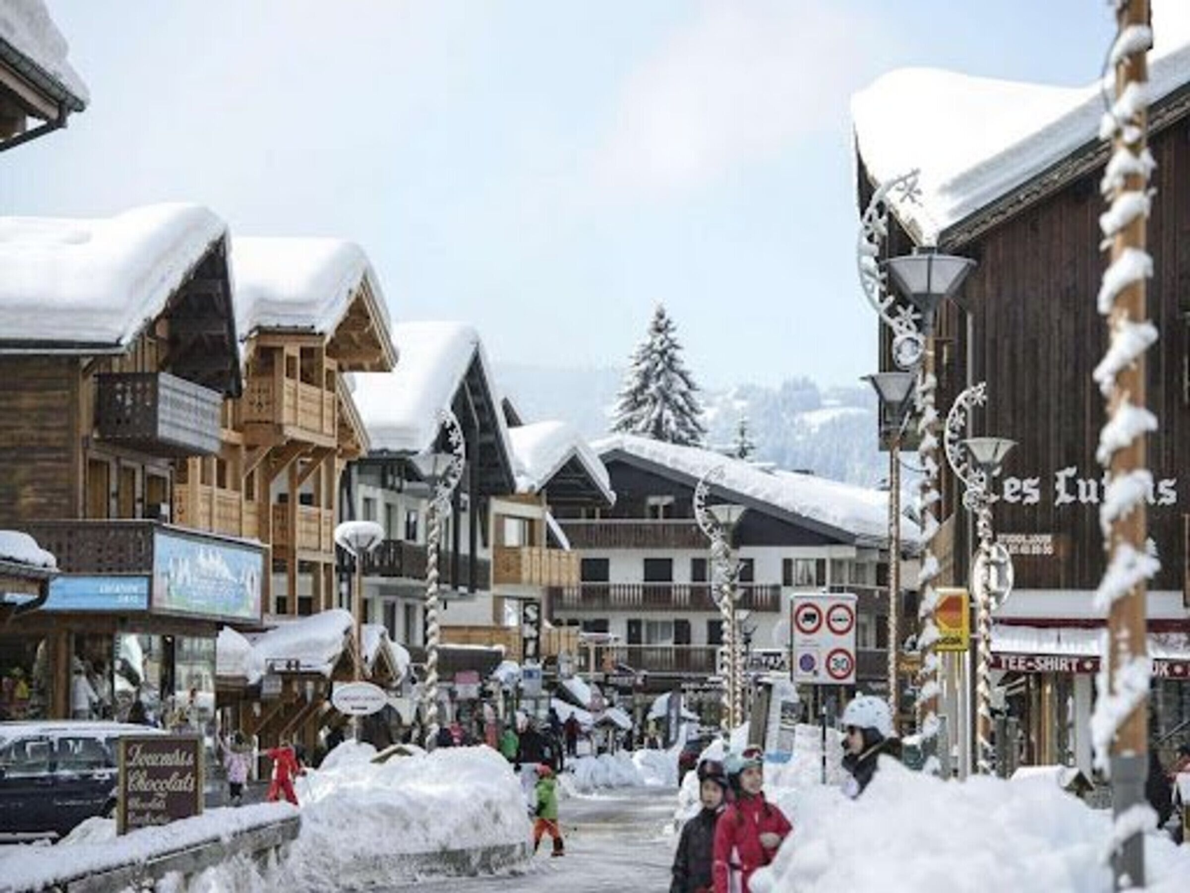 A snowy street with wooden buildings and a sign for "Les Lunes."