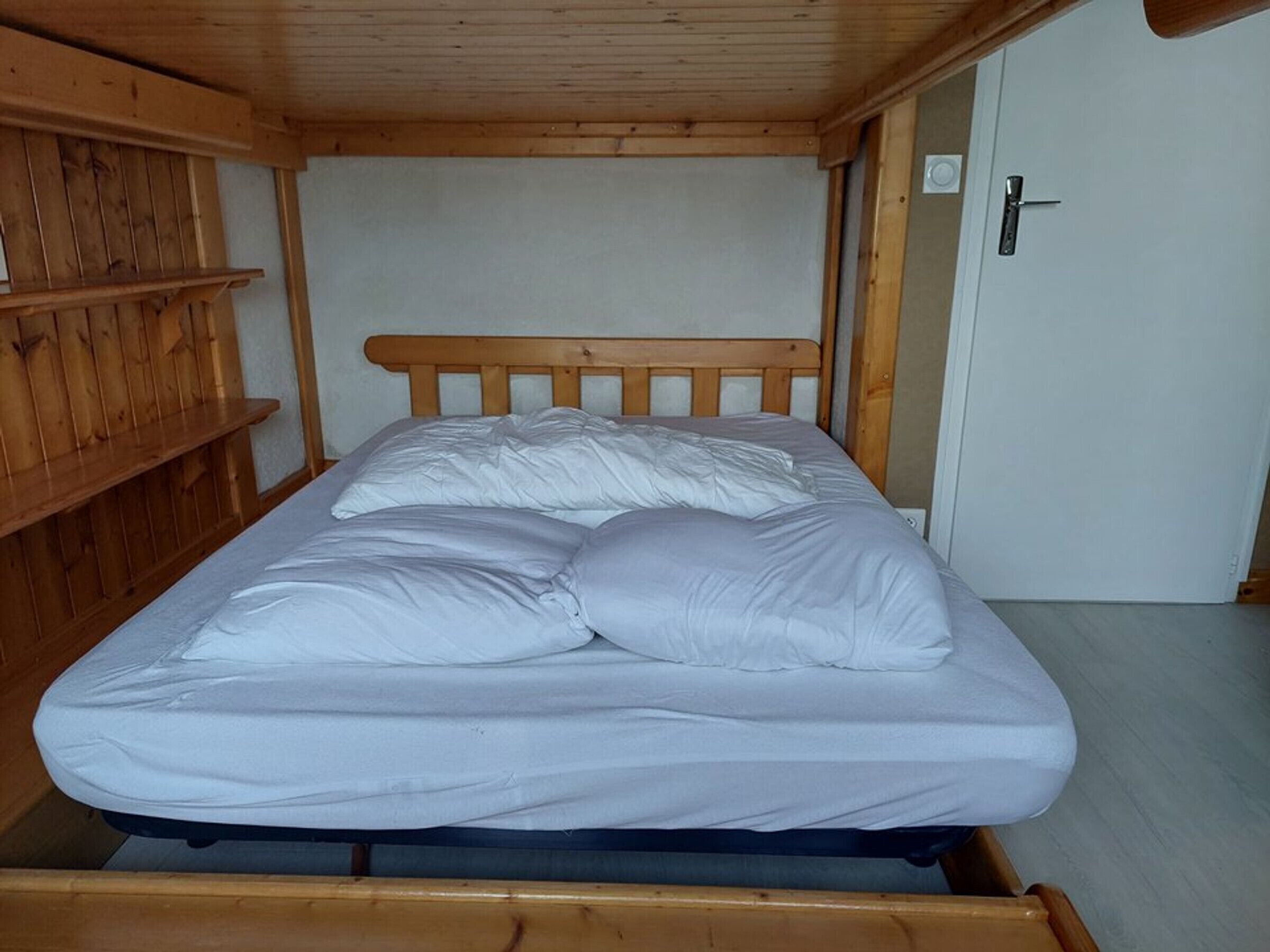 A single bed with a wooden headboard in a room with wooden walls and a door.