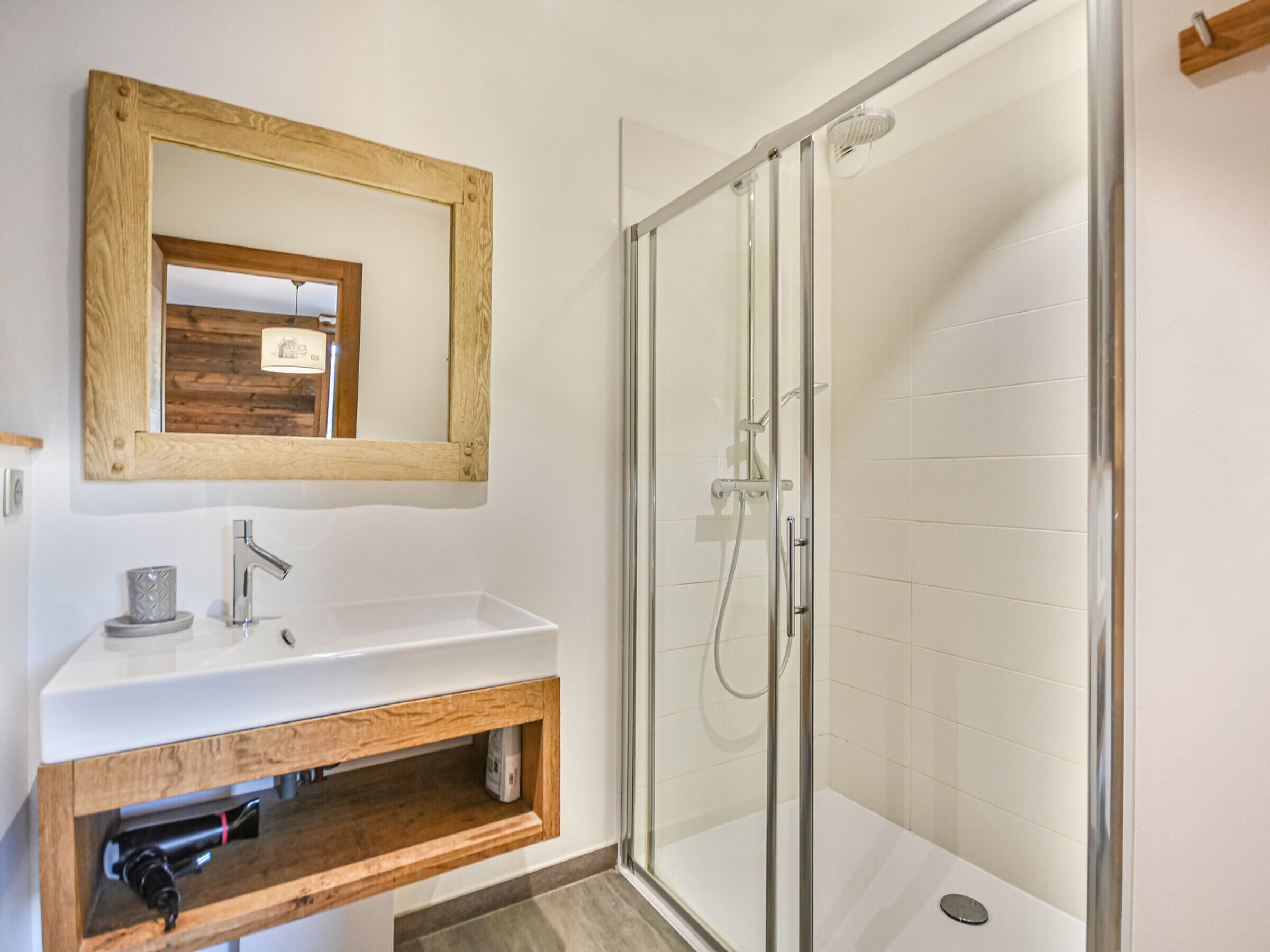 A bathroom with a wooden vanity, a mirror, a shower with glass doors, and white tiled walls.