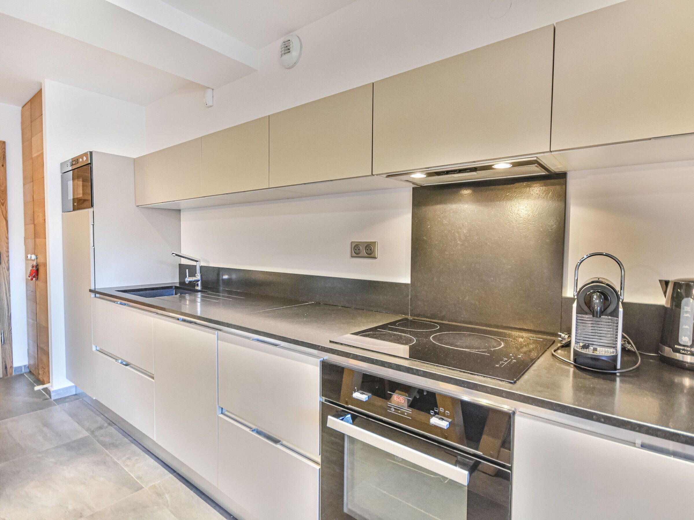 A modern kitchen with a stainless steel range hood, a built-in oven, and a coffee machine.