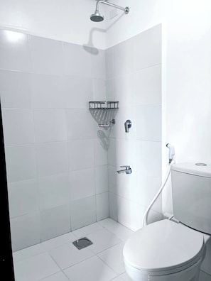 A small, white bathroom with a shower, toilet, and a small shelf.