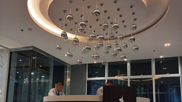 A modern reception area with a circular desk labeled "KASARA Urban Resort Residence," featuring a unique hanging light fixture and a glass elevator. - Cozy Nook in the City (Pasig)