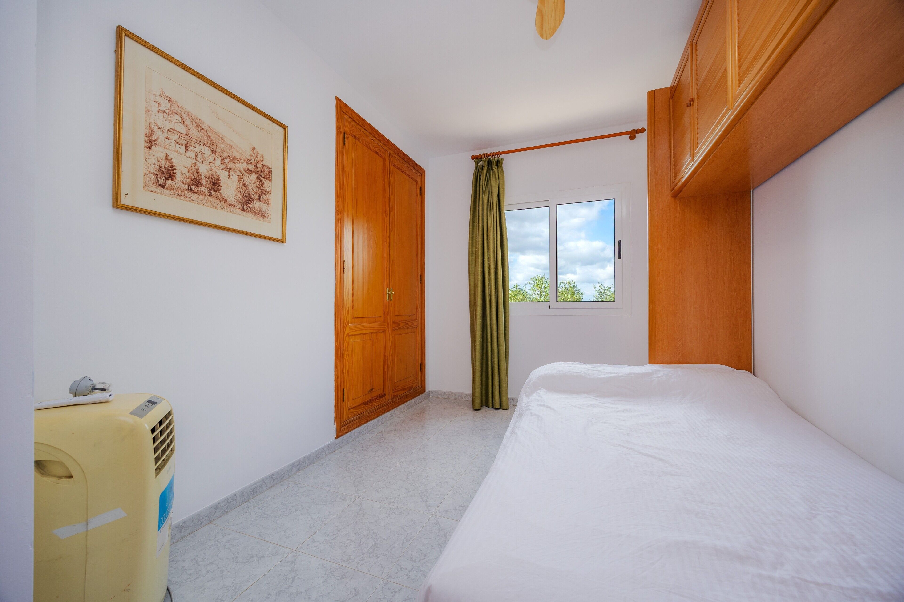 Un dormitorio con cama, armario de madera, ventana con cortinas y radiador.
