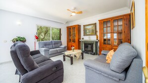 Ein Wohnzimmer mit Kamin, grauen Sofas, einem Couchtisch und einem Deckenventilator.