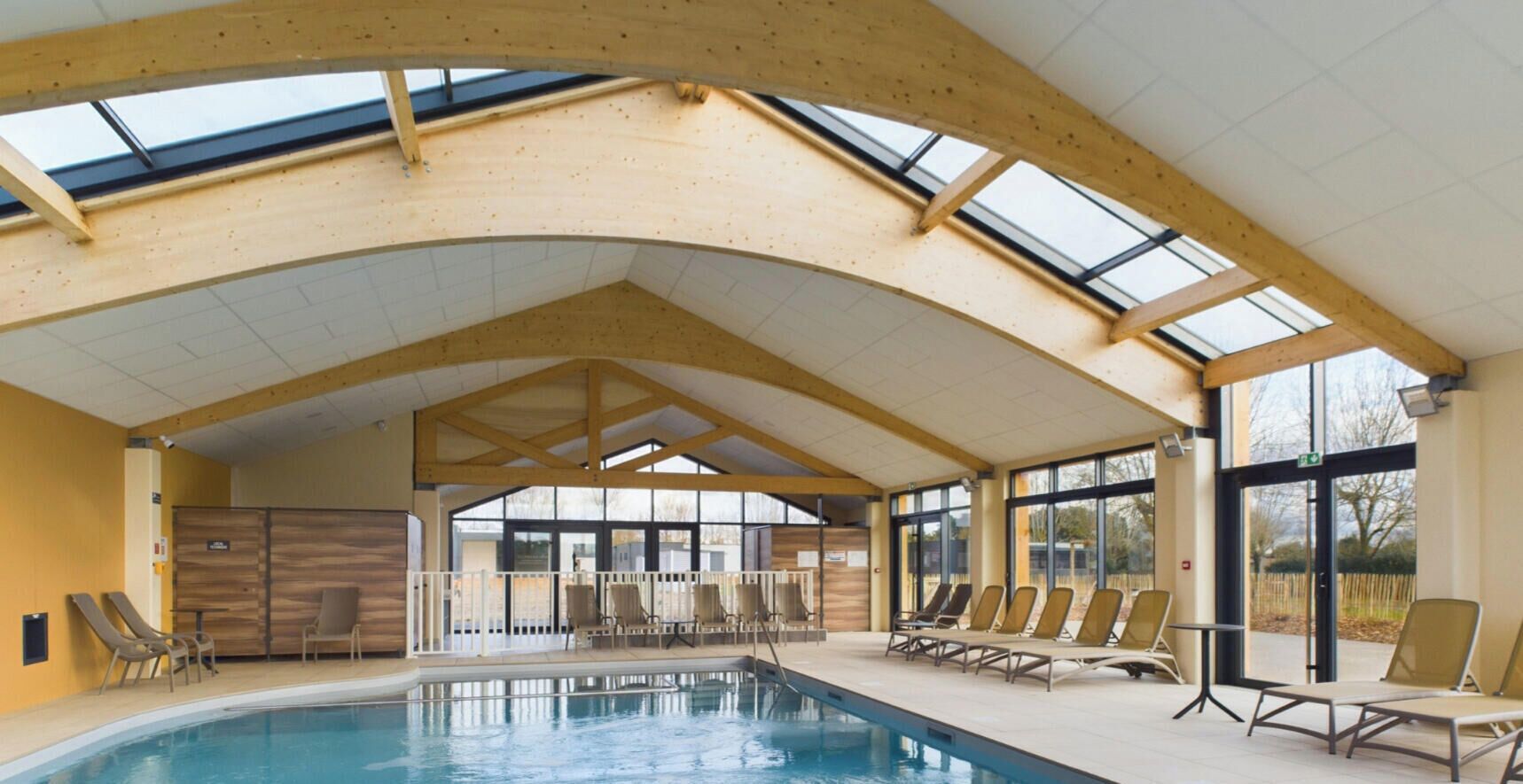 An indoor swimming pool with a wooden ceiling and large windows.