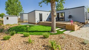 Ein modernes, zweistöckiges Haus mit überdachter Terrasse, kleinem Garten und Baum im Vordergrund.