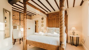 A four-poster bed with white linens, a small bedside table with a lamp, and a chair in a room with exposed brick walls and wooden beams. - Experience boutique comfort above The Powell pub in Birchington. Stylish en-suite rooms, luxury touches, and a vibrant pub below—perfect for business, couples, or families. Book your coastal escape today! (Birchington)