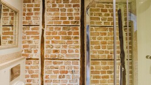 A bathroom with a brick wall, a glass shower enclosure, and a toilet. - Experience boutique comfort above The Powell pub in Birchington. Stylish en-suite rooms, luxury touches, and a vibrant pub below—perfect for business, couples, or families. Book your coastal escape today! (Birchington)