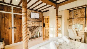 A bedroom with a brick fireplace, wooden beams, a bed with floral bedding, and a bathroom with a mirror and sink. - Experience boutique comfort above The Powell pub in Birchington. Stylish en-suite rooms, luxury touches, and a vibrant pub below—perfect for business, couples, or families. Book your coastal escape today! (Birchington)