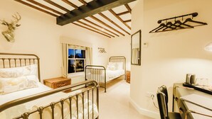 A bedroom with two beds, a wooden ceiling, a window with curtains, a mirror, and a desk with a chair.