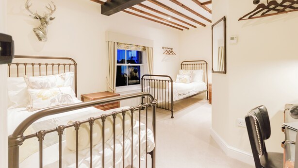 A bedroom with two beds, a wooden ceiling, a deer head decoration, and a window with curtains.