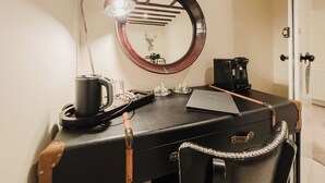 A compact workspace with a desk, a coffee maker, a lamp, and a mirror.