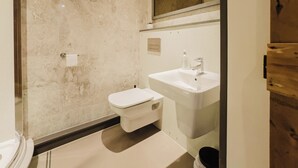 A modern bathroom with a marble wall, a toilet, a sink, and a mirror.