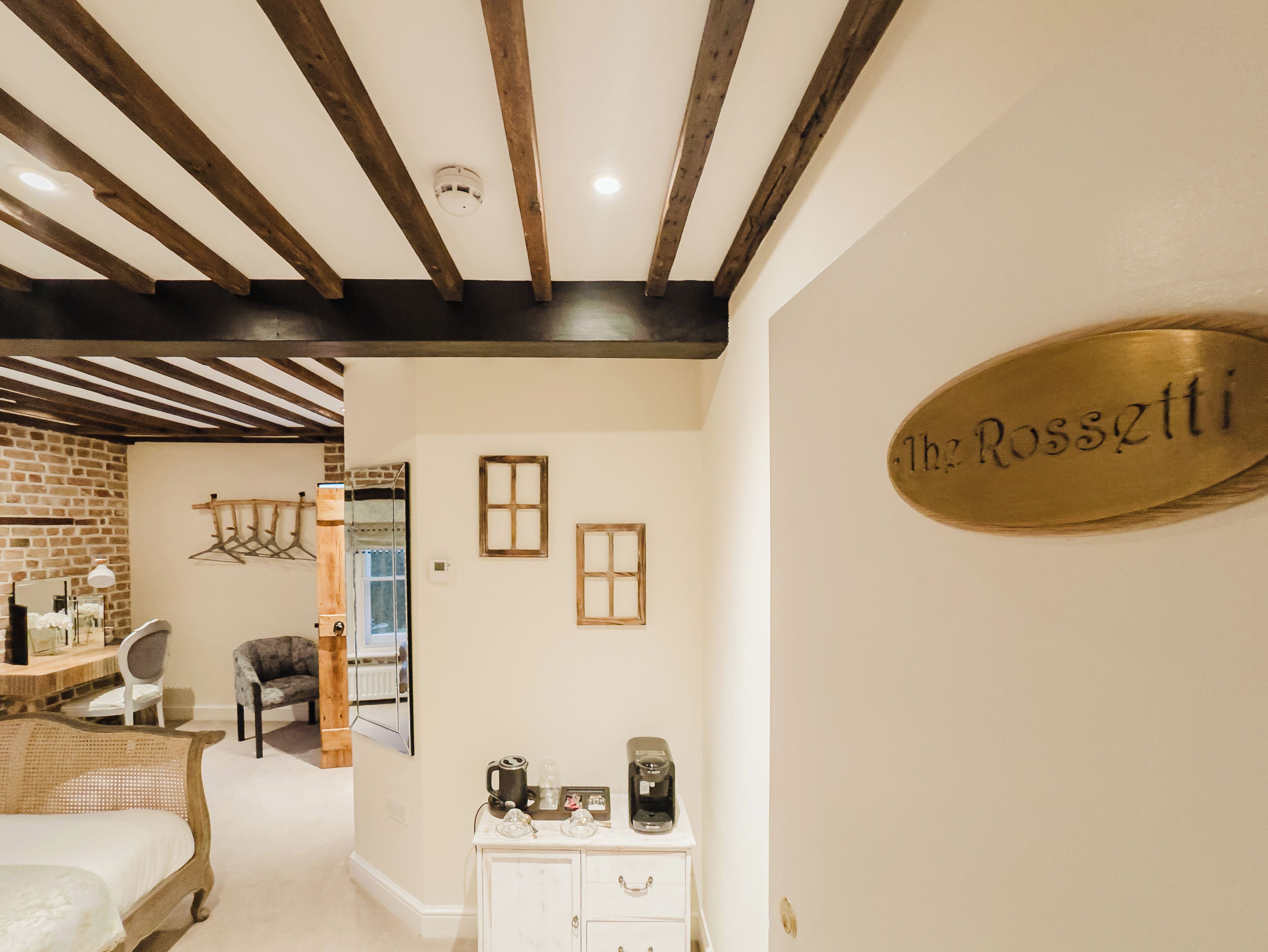 Camera d'albergo con travi a vista in legno, un letto, una cassettiera con macchinette da caffè e un cartello con su scritto 'The Rossztti'.