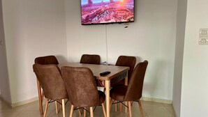 Un comedor con una mesa y seis sillas, un televisor montado en la pared y piso de baldosas.