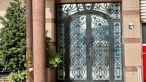 Una entrada de edificio con un portón metálico grande y ornamentado y un cartel encima.