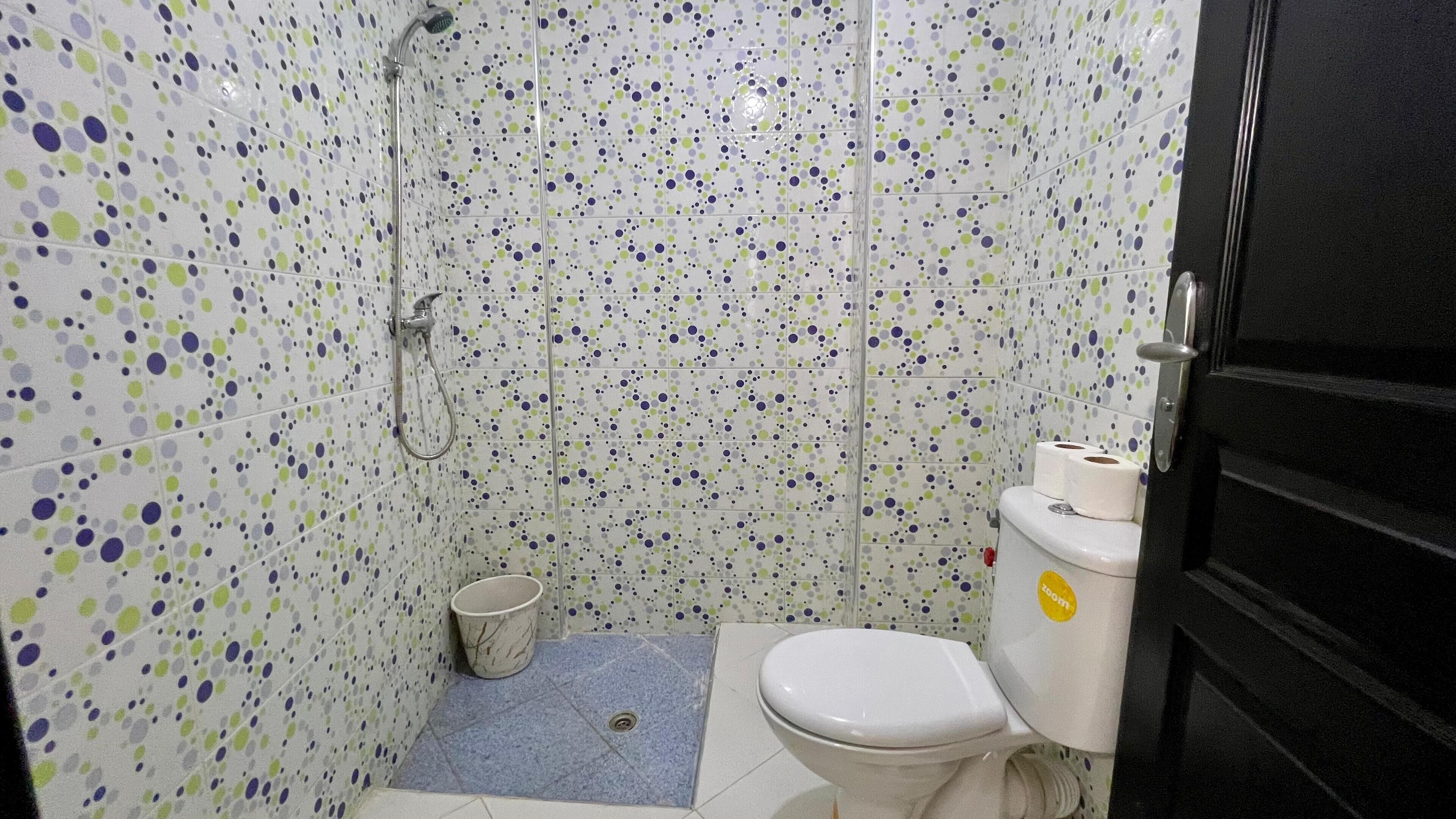 Een badkamer met toilet, douche en emmer.