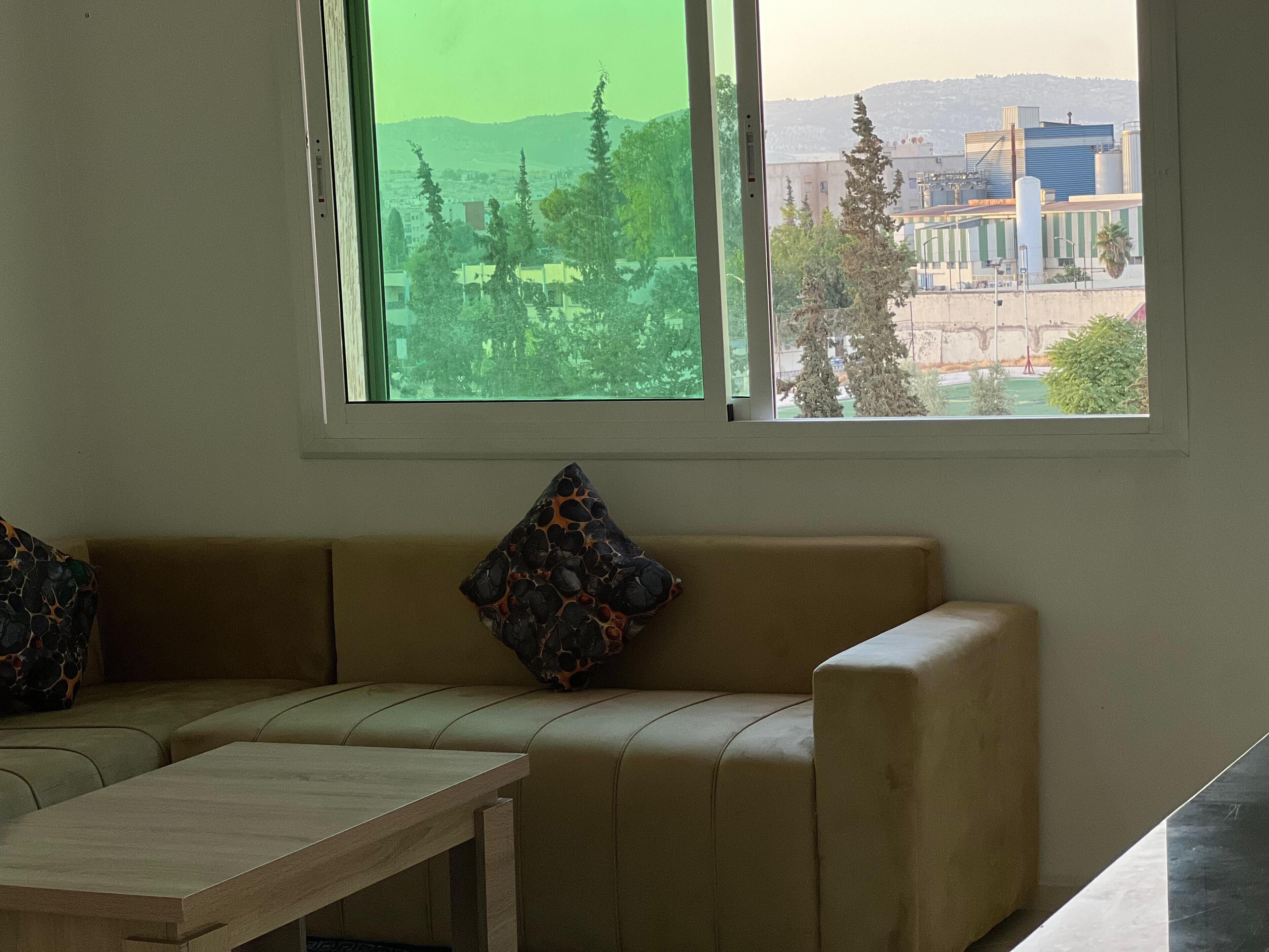 A room with a beige sofa, a small wooden table, and a window with a view of buildings and trees.