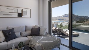 A modern living room with a large window, a sofa, and a view of a pool and mountains.