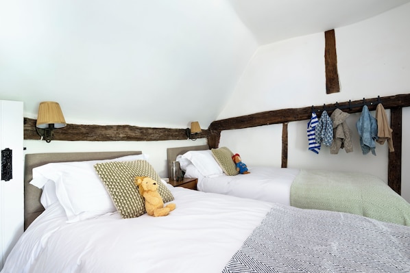 A bedroom with two beds, a wooden beam ceiling, a lamp, and a coat rack with clothes. - Gallops Cottage (Hassocks)