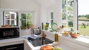 A bright kitchen with white cabinetry, a black microwave, a toaster, and a window overlooking a garden.