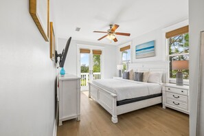 A bedroom with a bed, bedside tables, a ceiling fan, and a view of the outdoors.