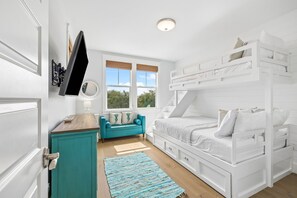 Un dormitorio con una cama litera, un sofá color turquesa, un televisor montado en la pared y una ventana con vistas a zonas verdes.