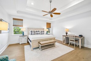 A bedroom with a bed, bedside tables, a desk, a chair, a bench, a ceiling fan, and a window with blinds.