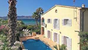 A yellow building with a pool, palm trees, and a view of the sea.