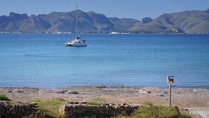 A coastal scene with a sailboat anchored in calm waters, a rocky shoreline, and distant mountains.