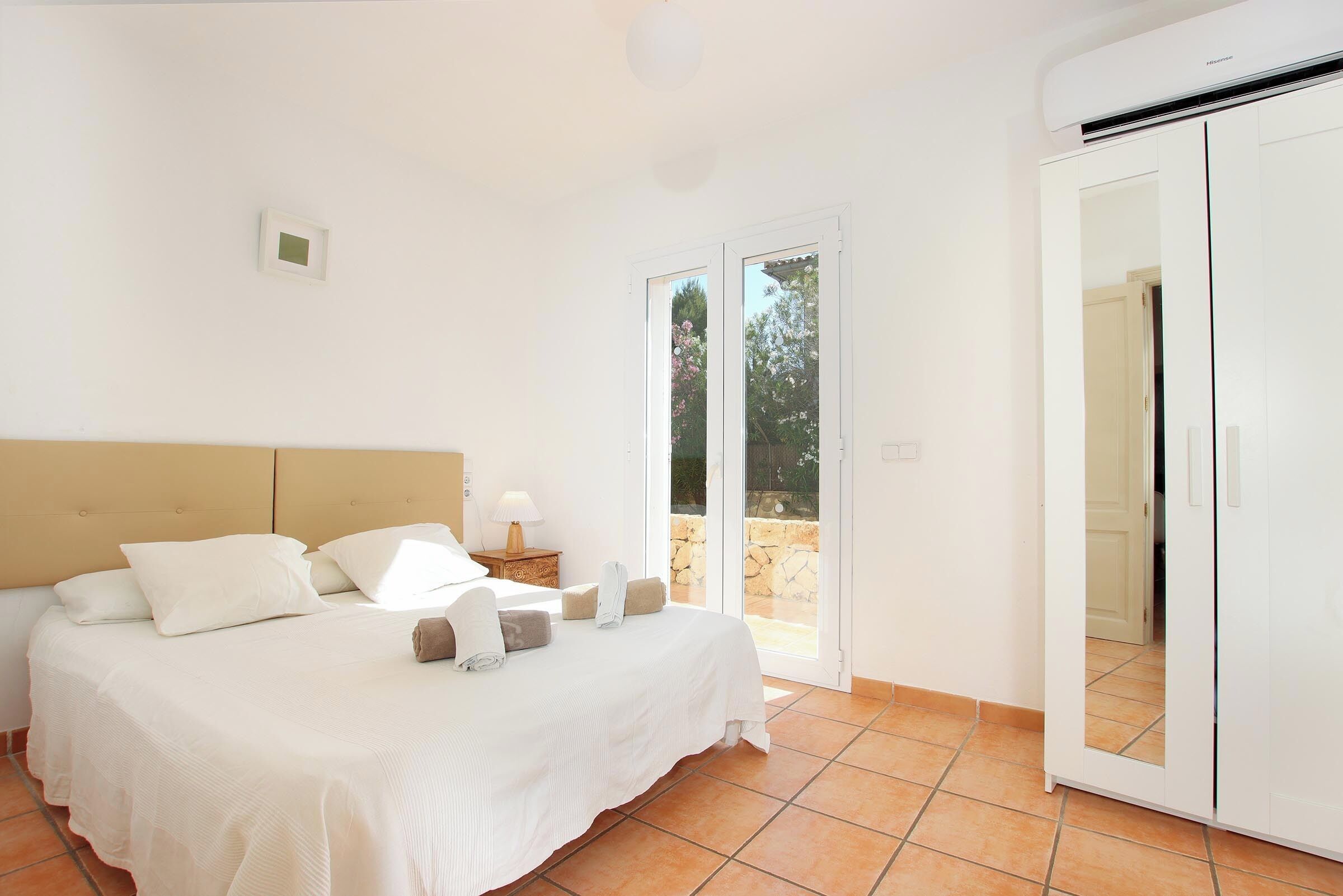 Une chambre à coucher comprenant un lit, une table de chevet, une lampe et une porte-fenêtre coulissante donnant sur un espace extérieur.