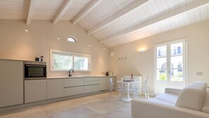 Une cuisine moderne dotée d’un four encastré, un coin repas avec une table et des chaises blanches, et un canapé blanc.