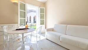 Une pièce avec un canapé blanc, une table ronde entourée de chaises transparentes et une bouteille posée sur la table.