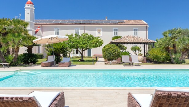 Une piscine avec des chaises longues, un bâtiment surmonté d’un dôme rouge et un ciel d’un bleu limpide.