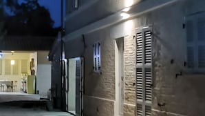 Un edificio con fachada de piedra, una puerta con contraventanas y un pequeño espacio al aire libre con una mesa y sillas.