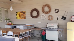 Una cocina con una mesa de madera, sillas, un refrigerador, una parrilla y varios utensilios de cocina.