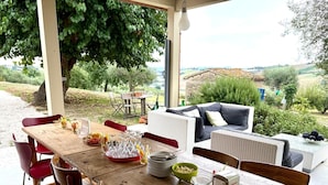 Un área de comedor al aire libre con mesa de madera, sillas rojas y sofá de mimbre.
