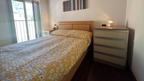 A bedroom with a bed, a nightstand, a dresser, and a window with blinds.