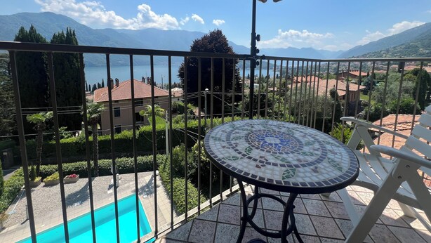 A balcony with a view of a lake, mountains, and a tiled pool area.