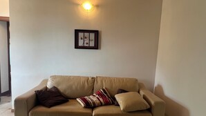 A beige sofa with multiple cushions, a framed picture on the wall, and a wall-mounted light fixture.