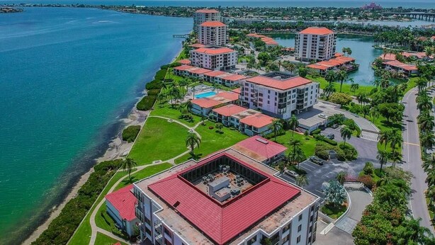 An aerial view of a coastal hotel complex with multiple buildings, a marina, and a bridge in the background. - Waterfront 2BR condo with pool, hot tub, gym, and balcony views. (St. Petersburg)