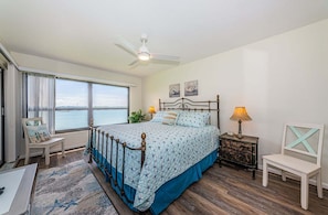A bedroom with a bed, a desk, a chair, a nightstand, a lamp, and a view of the water. - Waterfront 2BR condo with pool, hot tub, gym, and balcony views. (St. Petersburg)