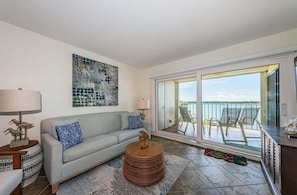 A living room with a sofa, a round wooden coffee table, and a large abstract painting on the wall. - Waterfront 2BR condo with pool, hot tub, gym, and balcony views. (St. Petersburg)