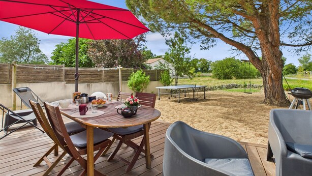 An outdoor patio with a round table, chairs, a red umbrella, and a large tree. - Colorful family home with garden for 6 (Longeville-sur-Mer)